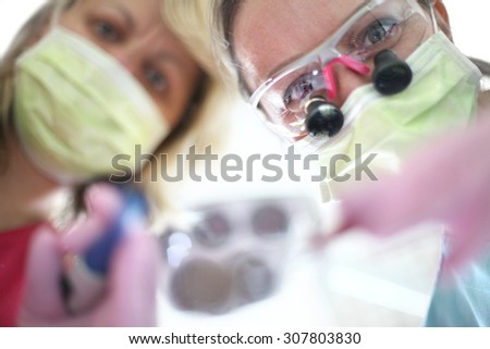 Becoming a patient in dentist office; female doctors\' faces covered with masks and protective eyeglasses with magnifying lens