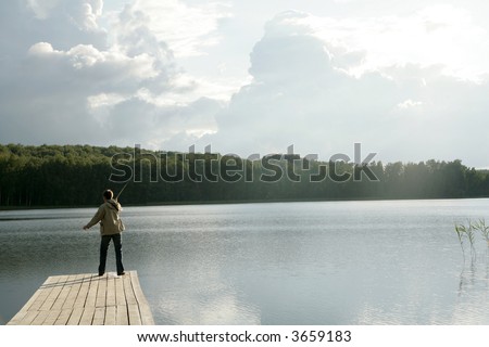 man standing on pier with back turned toward the camera fishing