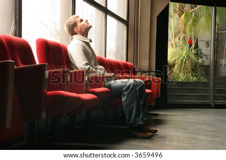 man sitting alone in one of many red chairs looking up
