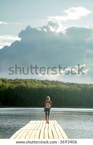 young woman walking on pier with big cloud overhead