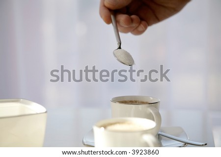 hand pouring spoon of sugar into cup of coffee