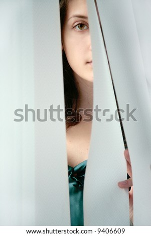 Girl enigmatically looking through the curtains