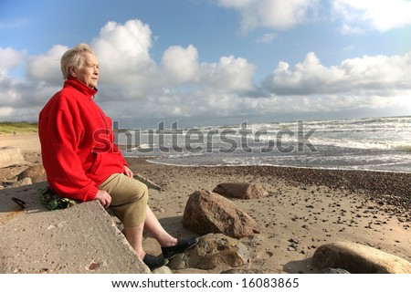 old woman sitting on the sea shore, looking at the sea and dreaming