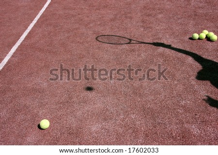 Red tennis court with yellow tennis balls and the shadow of a player