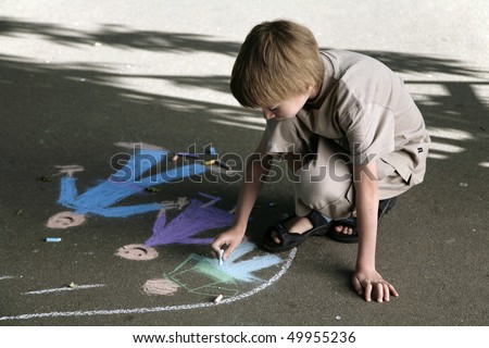 young boy draws the bright pieces of chalk on sidewalk