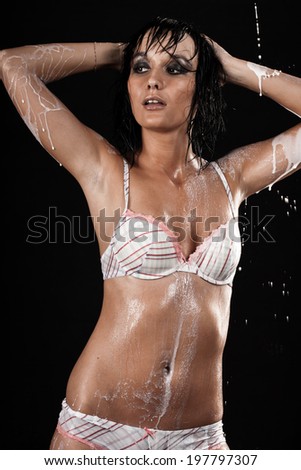 Wet girl in white bikini standing under a stream of milk