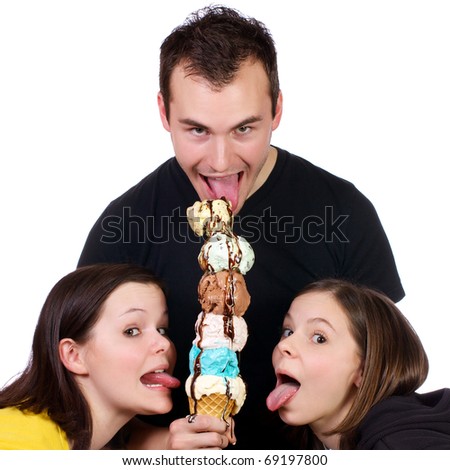 Three young adults licking huge six scoop ice cream cone with hot fudge careening down the ice cream and cone.