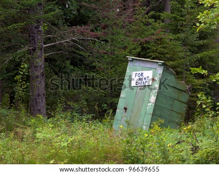 An old dilapidated out house in the woods with a sign on it 
