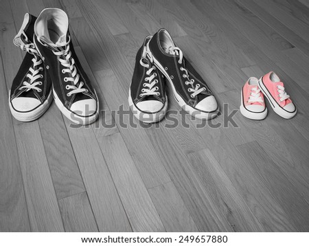 An image of two pairs of adults sneakers in black and white next to a baby pair of sneakers in pink