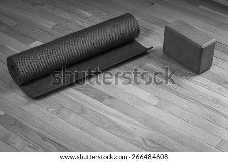 Black and white image of a yoga mat rolled up next to a yoga brick on a wood floor