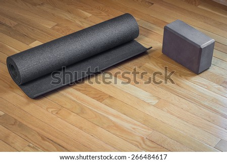 A black yoga mat rolled up next to a brown yoga mat on a wooden floor