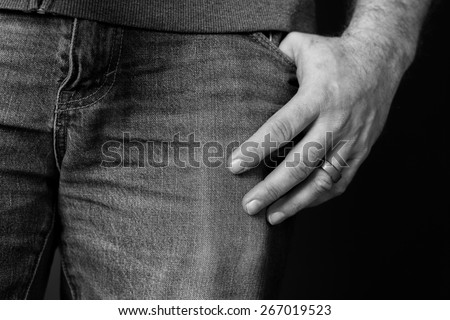 Black and white image of a detail of a man's left hand resting at the side of his pant leg with his thumb in his pocket