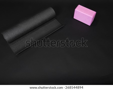 A black yoga mat with a pink yoga brick on a black background