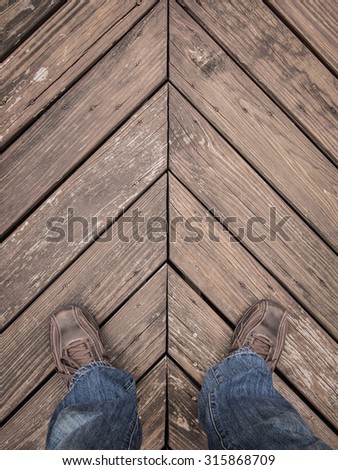 Color image of a man\'s legs and feet standing on a wooden deck