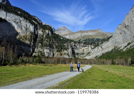 Two women and their dog walking in the alpine valley of Gasteretal, above Kandersteg, in Switzerland. Space for text in the sky.