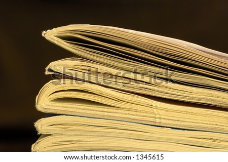 Macro of the end of a pile of old, yellowing magazines, set against a black background, with space for text.