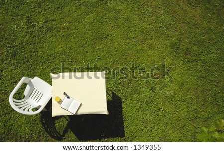 A garden chair, table, glass of orange juice, book and sunglasses, on a lawn. ready for the gardener to take a break. Vertical viewpoint. Space for text on the grass.