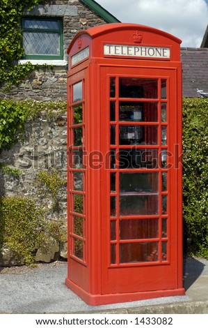 A well-kept British telephone box in a Welsh village. A Welsh stone cottage in the background.