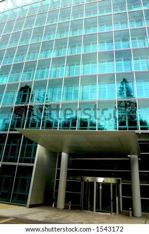 The deserted front door of an office block, trees reflected in the glass. One tree reflection appears to grow out of a pillar. Contrast between light at top of building and dark below.