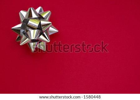 A decorative star, made from silver ribbon, on a plain red background with space for text (copy).
