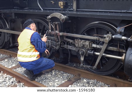 An driver oils the driving gear of his steam engine whilst the train is stopped in a station.