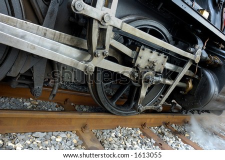 Detail of the drive gear of an old steam engine as it stands in a station, puffing steam, ready to go.