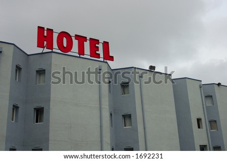 Grey walls, tiny windows, blocky architecture, all under a grey sky. The only bright thing about this hotel is its sign. Space for text in the sky.