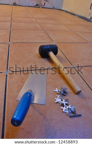 Close up of a workman's tools on a floor that is being tiled. More work in progress visible in background.