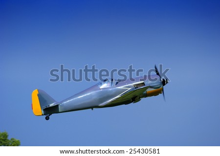 A single-seater aircraft taking off into a clear blue sky. Space for text in the sky.