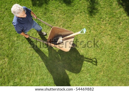 A gardener setting off to work with his wheelbarrow and tools, taken from a high viewpoint. Space for text to right and at base of image