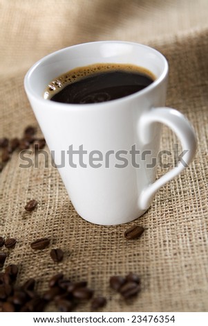 White coffee cup with roasted coffee beans on sackcloth. Shallow depth of field.