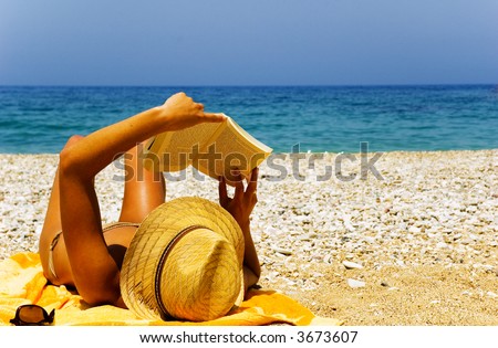 Beautiful girl relaxing by the seaside, reading a novel, in the sun.