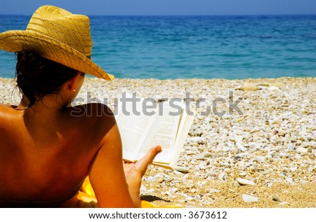 Beautiful girl relaxing by the seaside, reading a novel, in the sun.