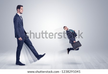 Big man in suit kicking out little himself with simple white wallpaper