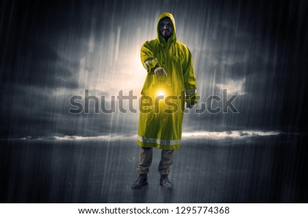 Raincoated man walking in storm with glowing lantern in his hand