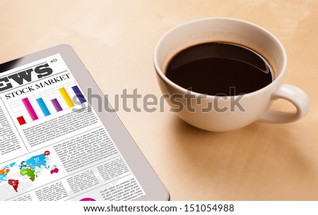 Workplace with tablet pc showing latest news and a cup of coffee on a wooden work table close-up