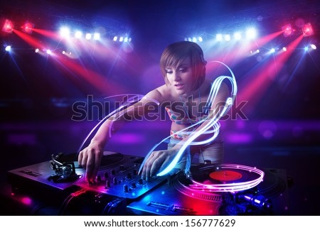 Pretty young disc jockey girl playing music with light beam effects on stage