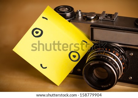 Drawn smiley face on a post-it note sticked on a photo camera