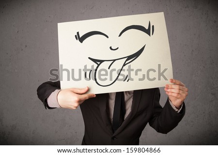 Young businessman holding a paper with funny smiley face on it in front of his head