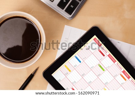 Workplace with tablet pc showing calendar and a cup of coffee on a wooden work table close-up