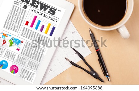 Workplace with tablet pc showing latest news and a cup of coffee on a wooden work table close-up