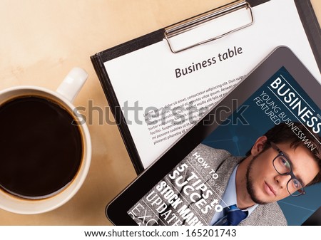 Workplace with tablet pc showing magazine cover and a cup of coffee on a wooden work table close-up