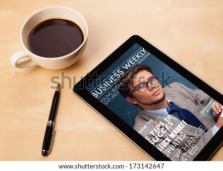 Workplace with tablet pc showing magazine cover and a cup of coffee on a wooden work table close-up
