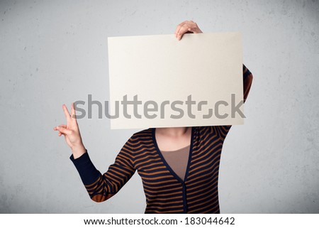 Woman standing and holding in front of her head a white paper with copy space