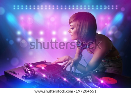 Pretty young disc jockey mixing music on turntables on stage with lights and stroboscopes