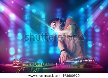 Young dj mixing music in a club with blue and purple lights