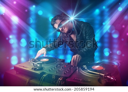 Young dj mixing music in a club with blue and purple lights