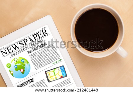 Workplace with tablet pc showing news and a cup of coffee on a wooden work table close-up
