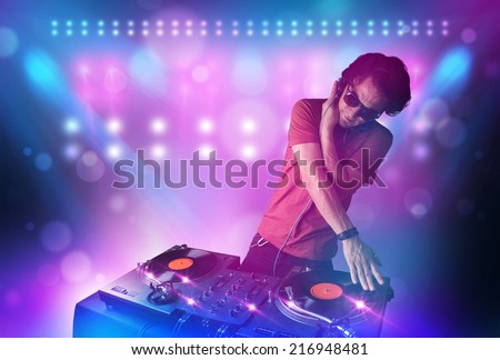 Young disc jockey mixing music on turntables on stage with lights and stroboscopes