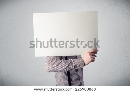 Businessman standing and holding in front of his head a white paper with copy space